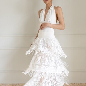 May include: A white halter top with a layered, white lace skirt. The skirt has a scalloped edge and fringe details.