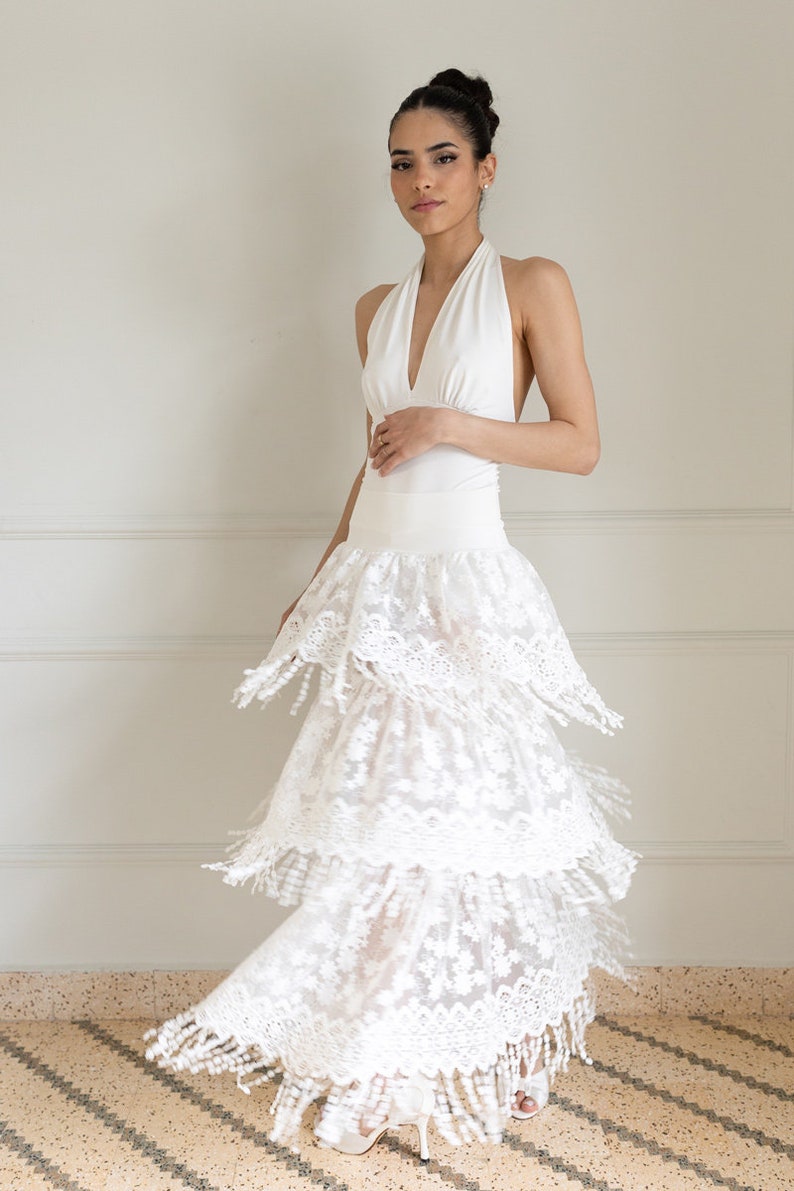 May include: A white halter top with a layered, white lace skirt. The skirt has a scalloped edge and fringe details.