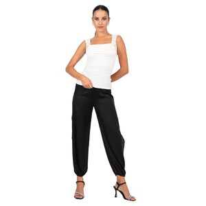 May include: A white sleeveless top with a square neckline and wide shoulder straps paired with black loose-fitting trousers that feature a tapered hem at the ankles. The outfit is completed with black heeled sandals that have thin straps.