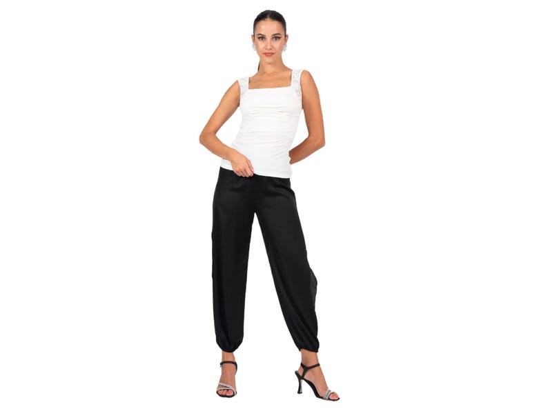 May include: A white sleeveless top with a square neckline and wide shoulder straps paired with black loose-fitting trousers that feature a tapered hem at the ankles. The outfit is completed with black heeled sandals that have thin straps.