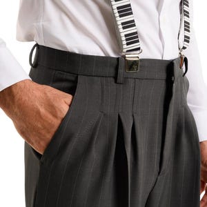 May include: Gray pinstripe dress pants with pleats and a waistband. The pants are being held up by black and white piano key suspenders.