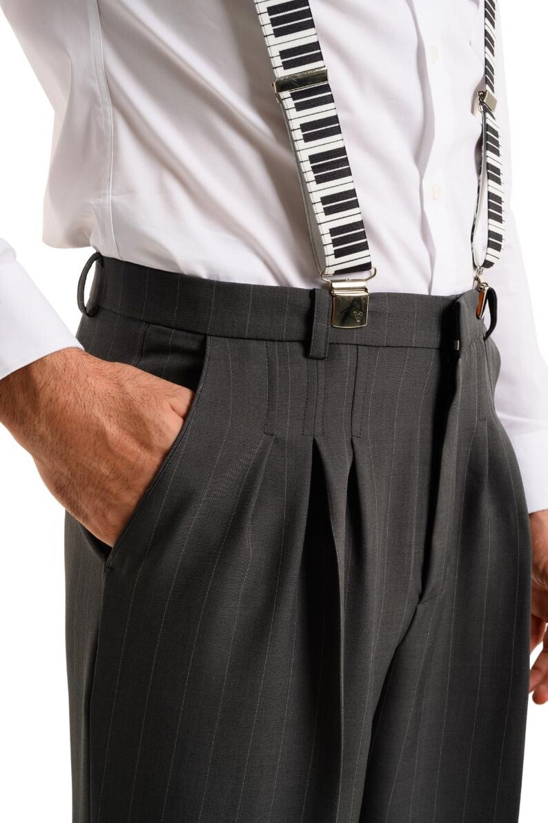 May include: Gray pinstripe dress pants with pleats and a waistband. The pants are being held up by black and white piano key suspenders.