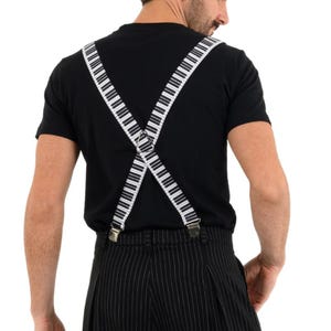 May include: A person wearing a black t-shirt with white piano key suspenders. The suspenders are crossed in the back and attached to black and white striped pants.