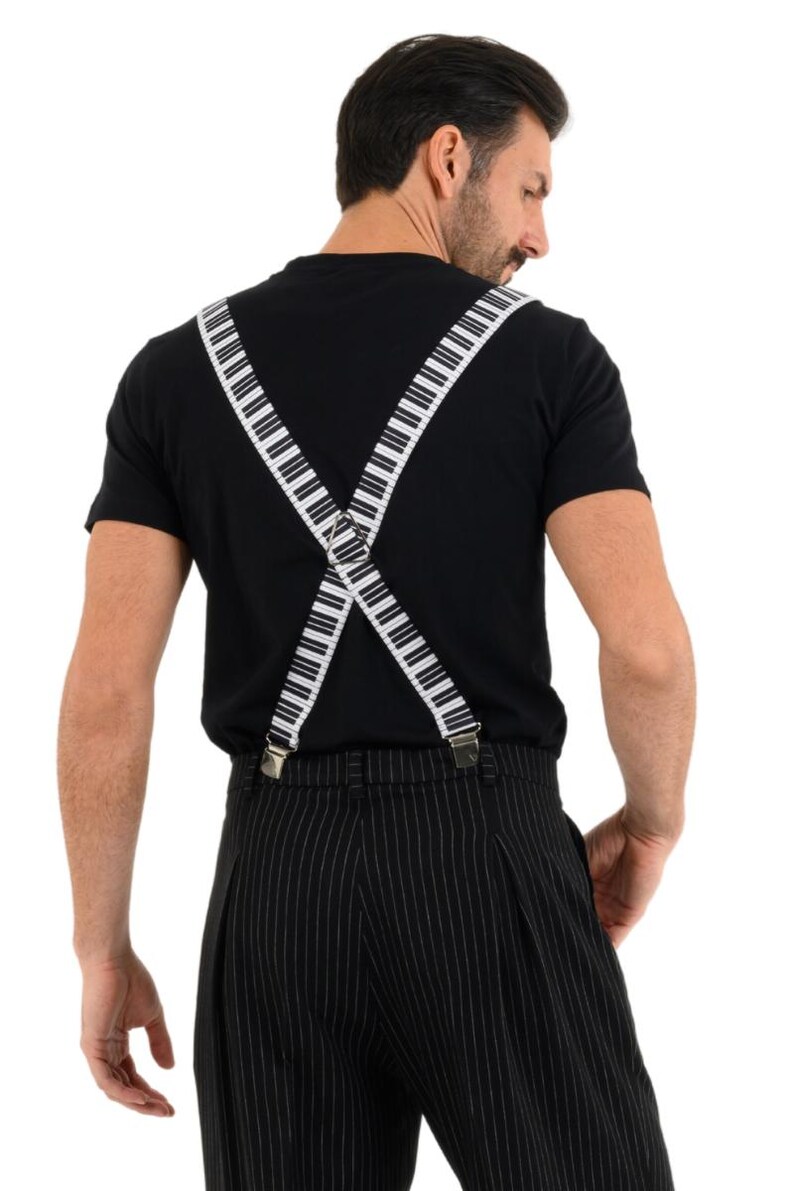 May include: A person wearing a black t-shirt with white piano key suspenders. The suspenders are crossed in the back and attached to black and white striped pants.