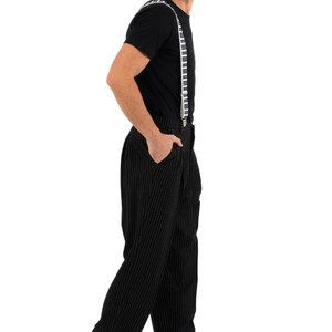 May include: A man wearing a black t-shirt with piano key suspenders and black pinstripe pants. He is wearing black shoes with white accents.