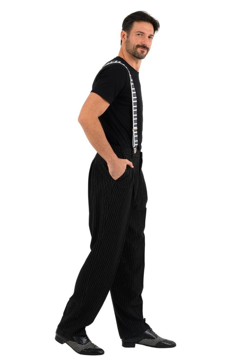 May include: A man wearing a black t-shirt with piano key suspenders and black pinstripe pants. He is wearing black shoes with white accents.
