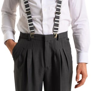 May include: A man wearing a white button-down shirt with black and white piano key suspenders and gray pinstripe pants.