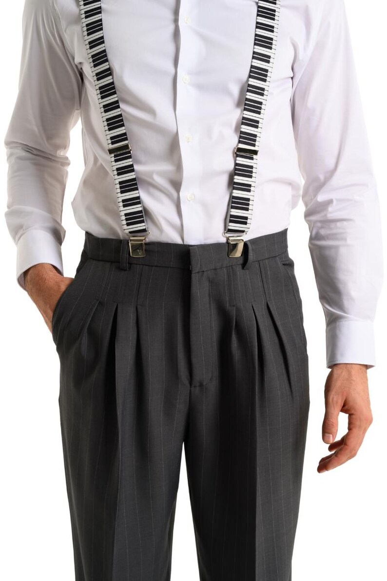 May include: A man wearing a white button-down shirt with black and white piano key suspenders and gray pinstripe pants.