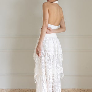 May include: A white halter top with a white lace skirt with fringe detailing. The skirt is layered and has a flowy silhouette.