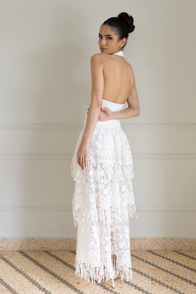 May include: A white halter top with a white lace skirt with fringe detailing. The skirt is layered and has a flowy silhouette.