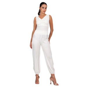 May include: A white sleeveless jumpsuit featuring a cowl neckline, a fitted bodice, and loose-fitting trousers with gathered elastic cuffs at the ankles. The garment is constructed from a solid white fabric with a subtle sheen and a smooth texture.