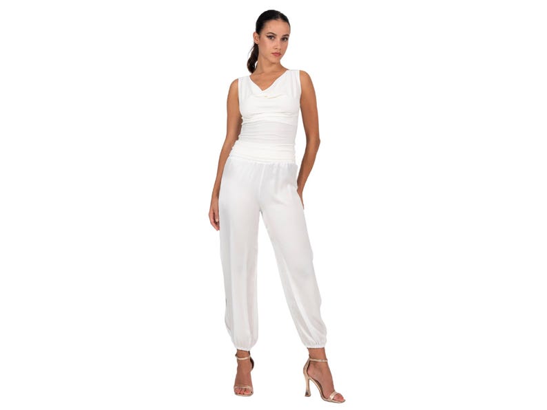 May include: A white sleeveless jumpsuit featuring a cowl neckline, a fitted bodice, and loose-fitting trousers with gathered elastic cuffs at the ankles. The garment is constructed from a solid white fabric with a subtle sheen and a smooth texture.