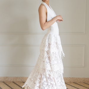 May include: A white halter top with a white lace skirt with fringe detailing. The skirt is layered and has a sheer look.