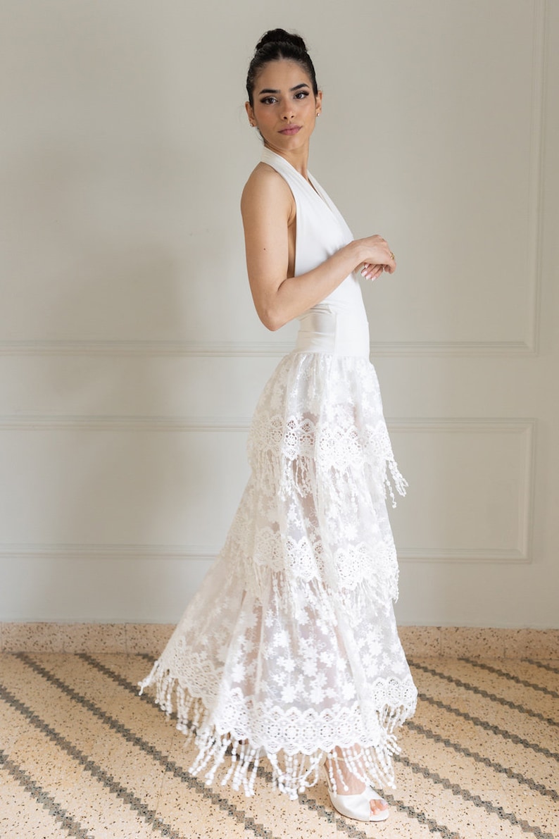 May include: A white halter top with a white lace skirt with fringe detailing. The skirt is layered and has a sheer look.