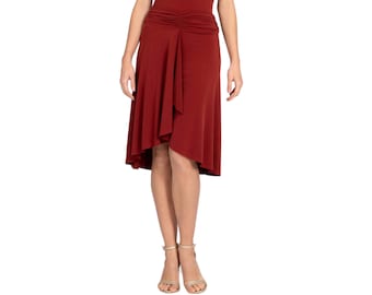 May include: A dark red skirt featuring a high-low hemline and a gathered, ruched detail at the center of the waistband. The skirt has a smooth, flowing fabric construction that drapes down to the knees, creating a layered effect with the front panel.