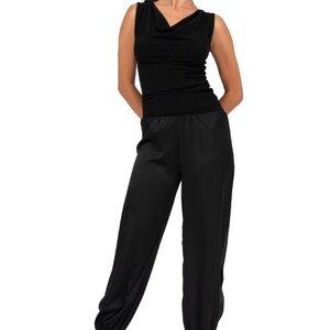 May include: A black sleeveless jumpsuit featuring a cowl neckline and a fitted bodice. The lower portion consists of loose-fitting trousers with elasticized cuffs at the ankles. The garment is solid black and has a smooth, uniform texture throughout.