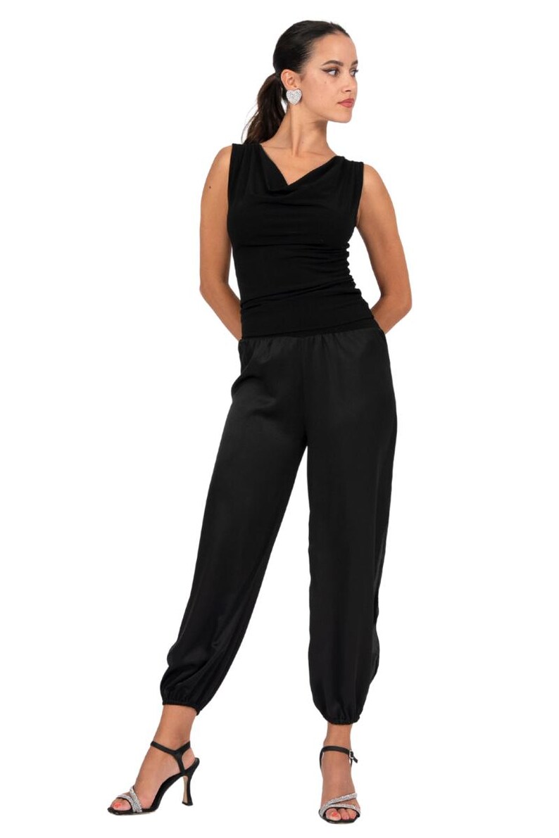 May include: A black sleeveless jumpsuit featuring a cowl neckline and a fitted bodice. The lower portion consists of loose-fitting trousers with elasticized cuffs at the ankles. The garment is solid black and has a smooth, uniform texture throughout.