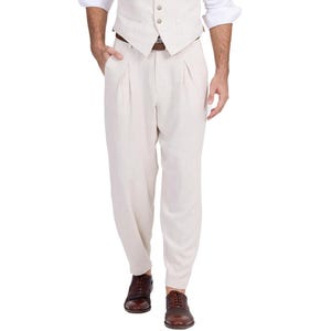 May include: A pair of beige linen pants with pleats. The pants have a relaxed fit and are worn with a brown leather belt.
