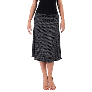 May include: A navy blue midi skirt with a white polka dot pattern. The skirt has a flared hem and is paired with a black top. The model is wearing gold-coloured sandals.