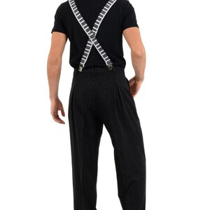 May include: A man wearing a black t-shirt with white piano key suspenders and black pinstripe pants.