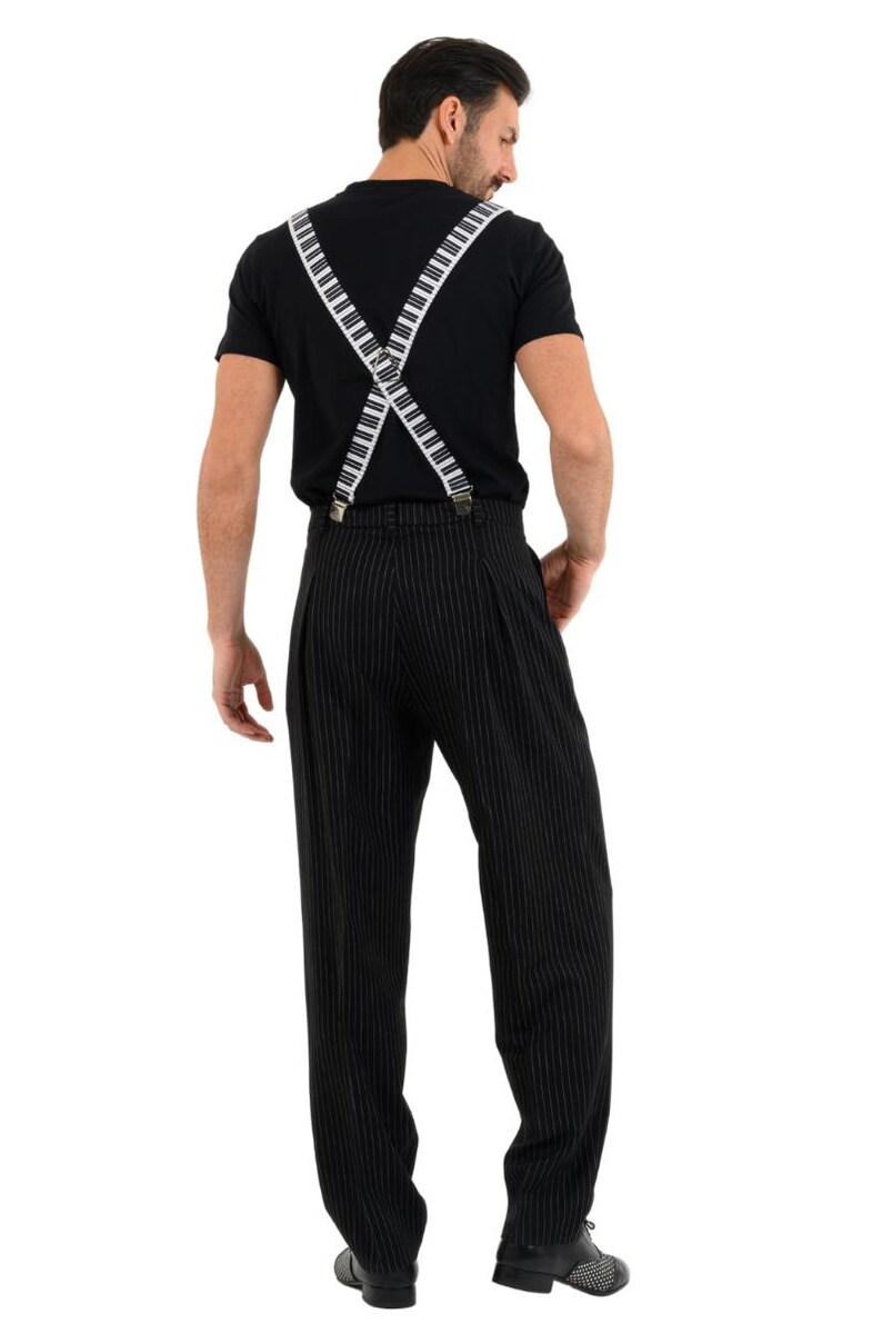 May include: A man wearing a black t-shirt with white piano key suspenders and black pinstripe pants.