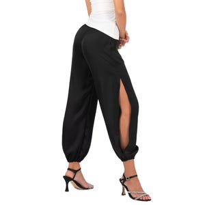 May include: Black trousers featuring a high-waisted design and wide legs with long vertical side slits that extend from the hip to the hem. The pants have gathered elastic cuffs at the ankles, creating a voluminous silhouette in a smooth fabric.