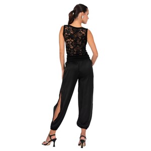May include: A sleeveless black top featuring a detailed floral lace back panel paired with matching black trousers that have a high-waisted fit, a smooth satin-like finish, and long vertical slits along the outer sides of the legs.