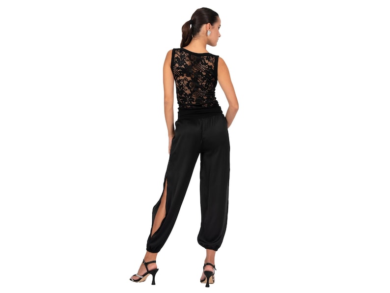 May include: A sleeveless black top featuring a detailed floral lace back panel paired with matching black trousers that have a high-waisted fit, a smooth satin-like finish, and long vertical slits along the outer sides of the legs.