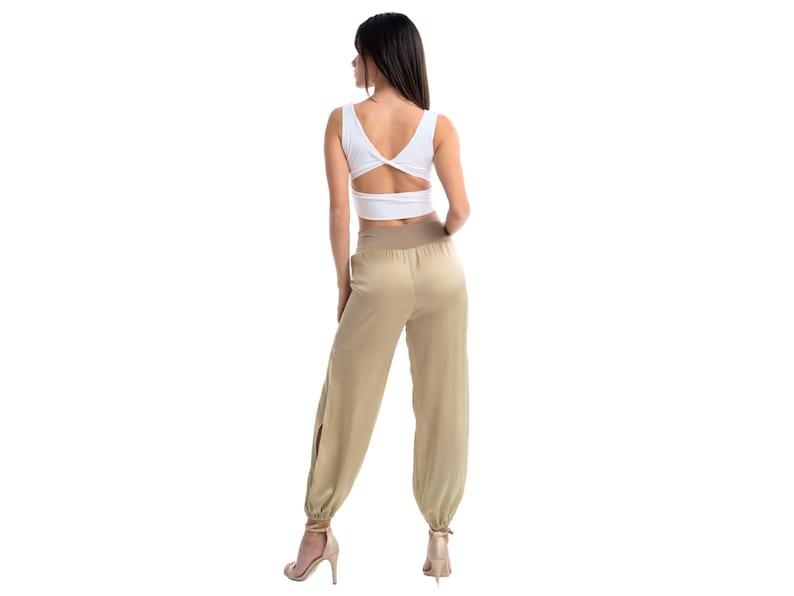 May include: A white sleeveless crop top with a V-neckline and a twisted back detail paired with high-waisted beige trousers featuring a wide elastic waistband, a relaxed fit, side leg slits, and gathered elastic cuffs at the ankles.