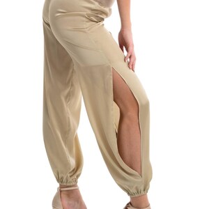 May include: Champagne-colored satin trousers featuring a high-rise elasticized waistband and dramatic side slits that extend from the hip to the ankle. The pants have a relaxed fit with gathered, elasticized cuffs at the bottom hem.