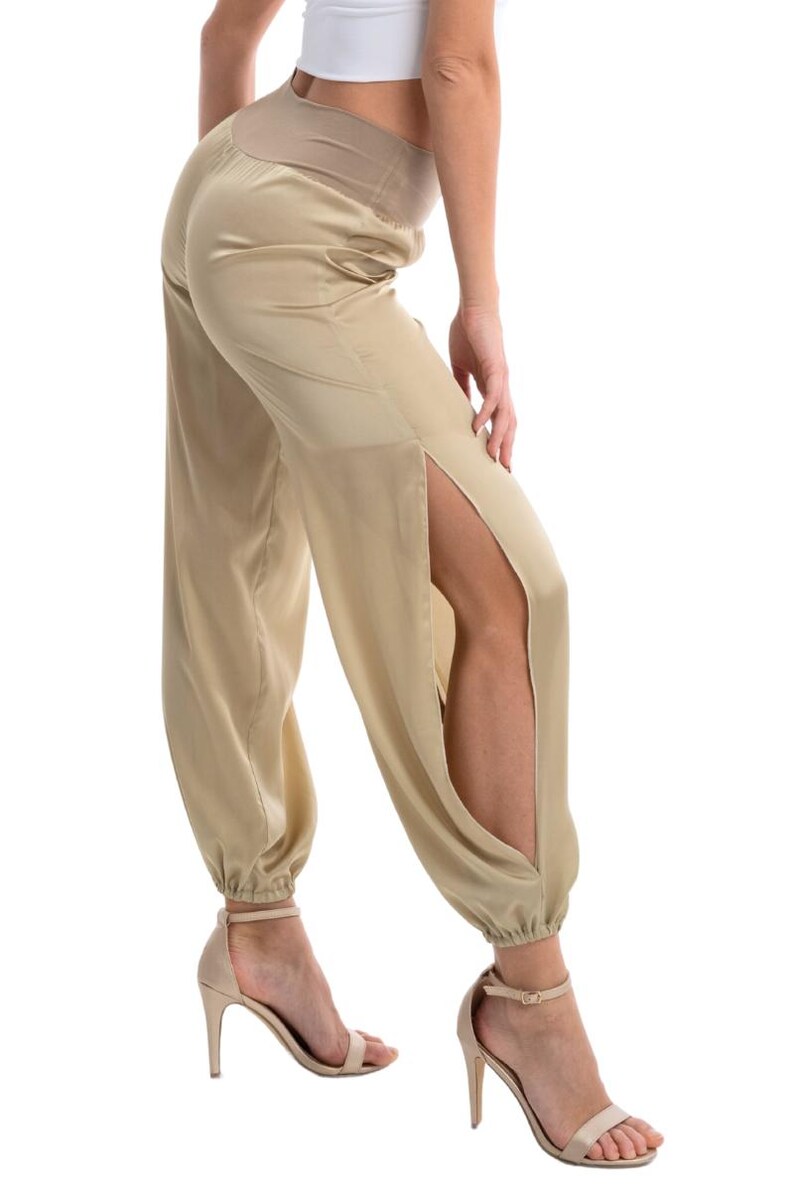 May include: Champagne-colored satin trousers featuring a high-rise elasticized waistband and dramatic side slits that extend from the hip to the ankle. The pants have a relaxed fit with gathered, elasticized cuffs at the bottom hem.