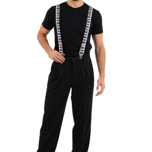 May include: A man wearing a black t-shirt and black pinstripe pants with white piano key suspenders.