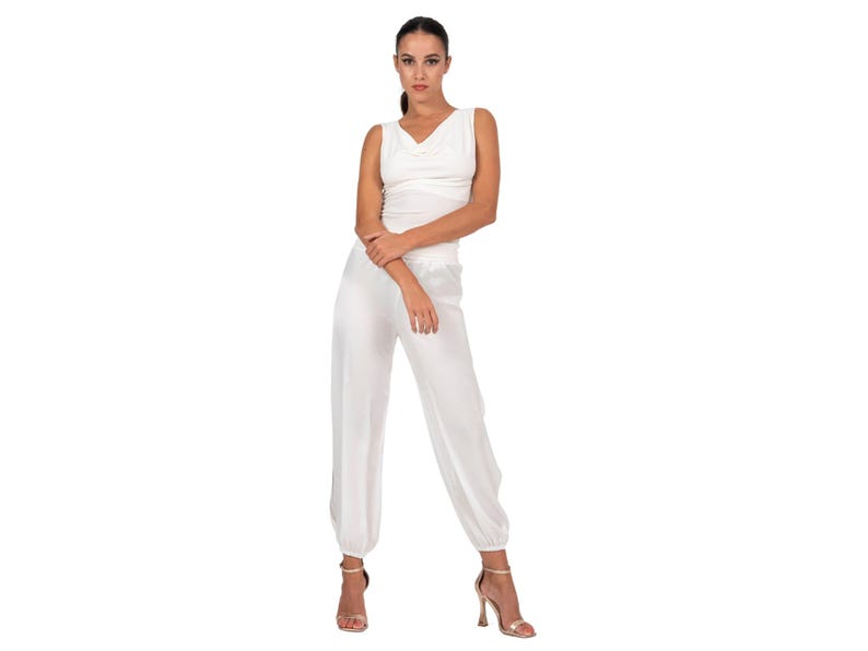 May include: A white sleeveless jumpsuit featuring a cowl neckline and a fitted bodice that transitions into loose-fitting, tapered trousers with gathered elasticized cuffs at the ankles. The garment is made of a smooth, solid white fabric.