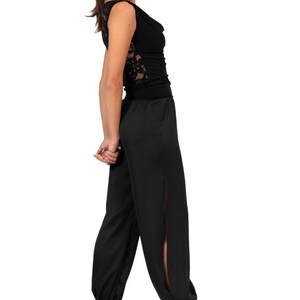 May include: A black sleeveless top featuring a cowl neckline and intricate lace side panels, paired with matching black loose-fitting trousers that have side slits and elasticized cuffs at the ankles, worn with black strappy high-heeled sandals.