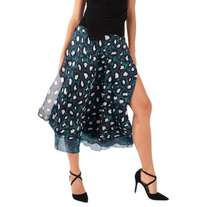 Può includere: Un top nero abbinato a una gonna fluida con un motivo a pois verde acqua e bianco. La gonna ha uno spacco alto e l'outfit è completato da tacchi neri.