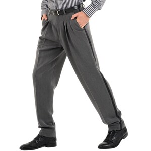 May include: Gray pleated pants with a black stripe down the side. The pants have a belt loop and a zipper fly.