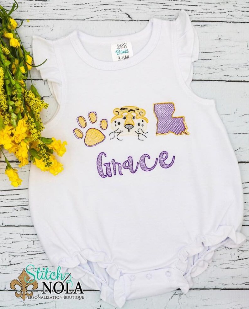 May include: White baby onesie with purple and yellow embroidery. The embroidery includes a paw print, a tiger face, the state of Louisiana, and the name "Grace".