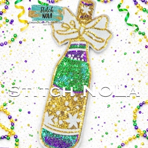 May include: A decorative champagne bottle-shaped applique with a white bow and gold accents. The bottle is embellished with green, gold, and purple beads. The text "Stitch NOLA" is displayed on the image.