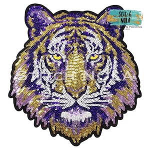 May include: A sequined tiger head patch in purple, gold, and white. The patch has a black border and the text "Stitch NOLA" is visible. The tiger's eyes are yellow.