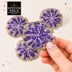 May include: Three circular embroidered patches featuring a purple sequined pom-pom design with gold glitter borders. The patches are arranged with one held in the foreground, displaying intricate stitching and a vibrant purple and gold color scheme.