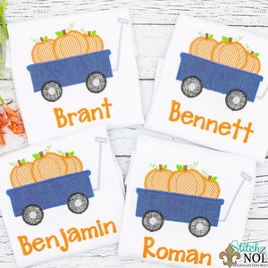 Puede incluir: Cuatro camisetas blancas con un carro azul y calabazas naranjas bordadas. Cada camiseta tiene un nombre diferente bordado: Brant, Bennett, Benjamin y Roman.