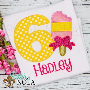 May include: A white t-shirt with a yellow number six with white polka dots, a pink and yellow popsicle with a pink bow, and the name Hadley in pink lettering.