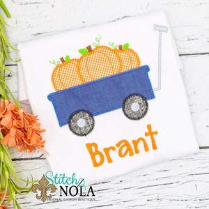 Puede incluir: Un carro azul con tres calabazas naranjas dentro. El carro tiene ruedas negras y un mango gris. El nombre "Brant" est&aacute; escrito en naranja debajo del carro.