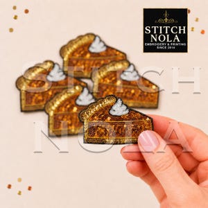May include: A collection of pumpkin pie slice patches featuring gold sequins and a white beaded dollop of whipped cream on top. The patches are triangular with a crust edge and a dark outline. One patch is held up in the foreground for detail.