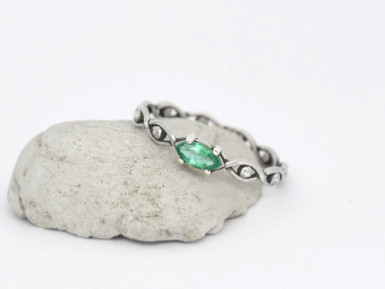 May include: A silver ring with a green marquise-shaped gemstone set in a delicate, twisted band.