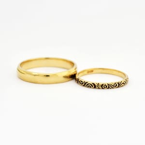 May include: Two gold wedding bands. One band is plain and the other has a delicate floral design.