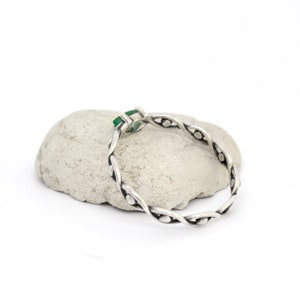 May include: A silver ring with a green gemstone set in a twisted band.