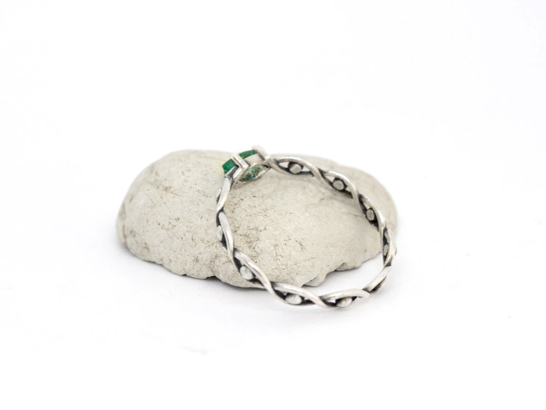 May include: A silver ring with a green gemstone set in a twisted band.