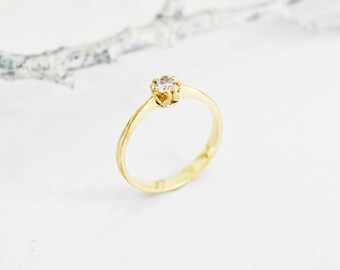 May include: A simple gold band ring with a single, small, round diamond set in a four-prong setting.