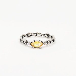 May include: A silver ring with a braided band and a yellow gemstone in the center.